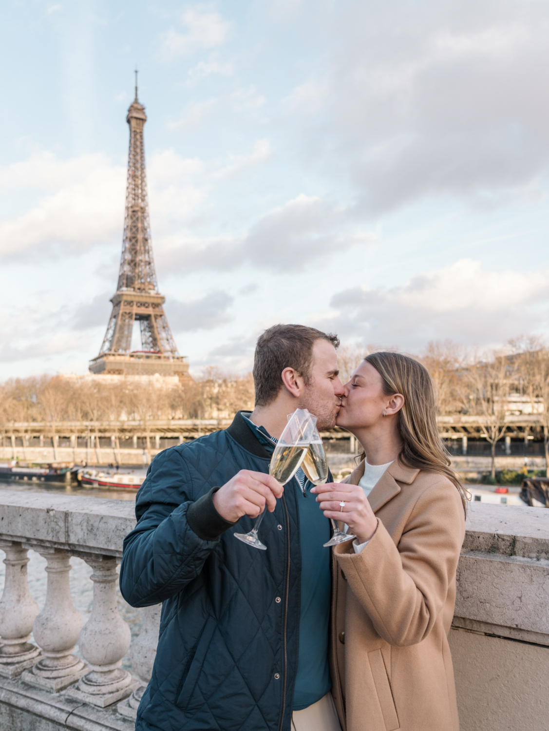 newly engaged couple kiss and hold champagne with view of eiffel tower in paris