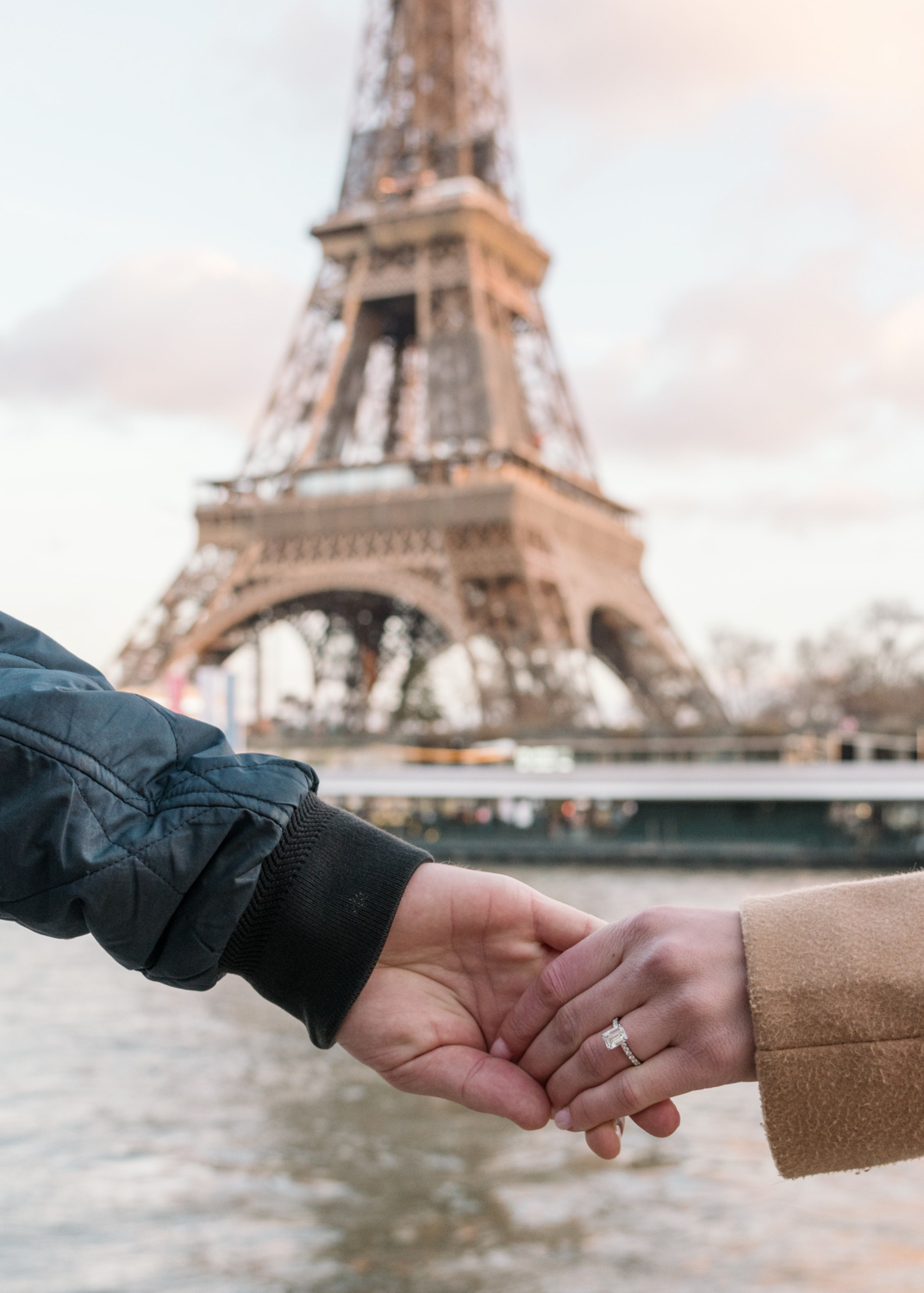 couple hold hand and show off engagement ring in front of eiffel tower