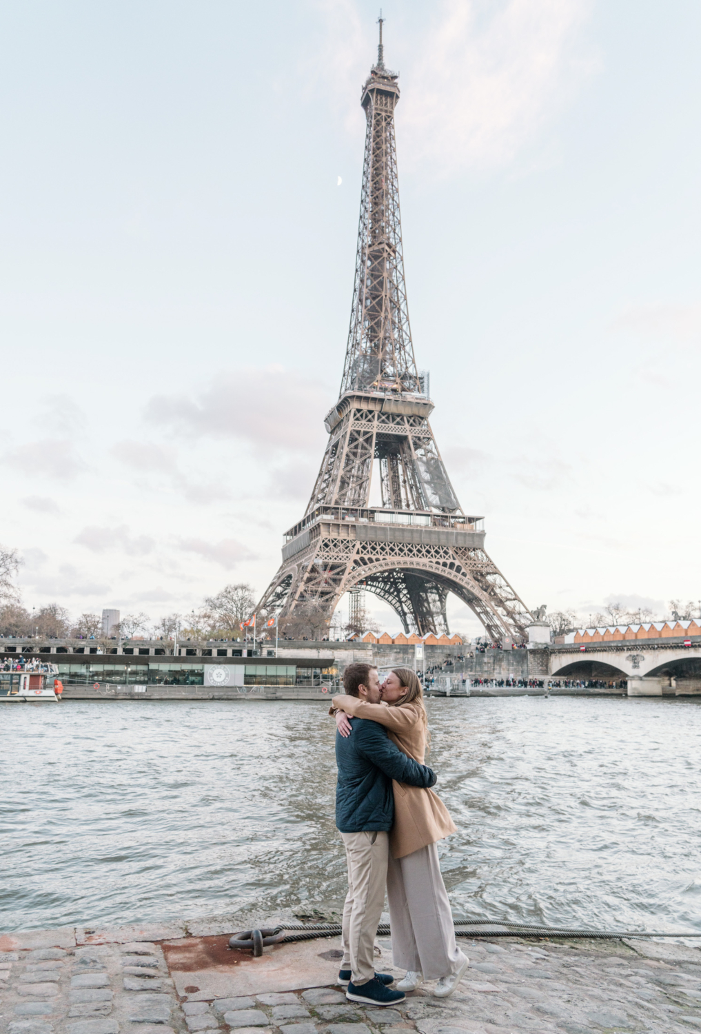 newly engaged couple wrap their arms around each other and kiss with view of eiffel tower