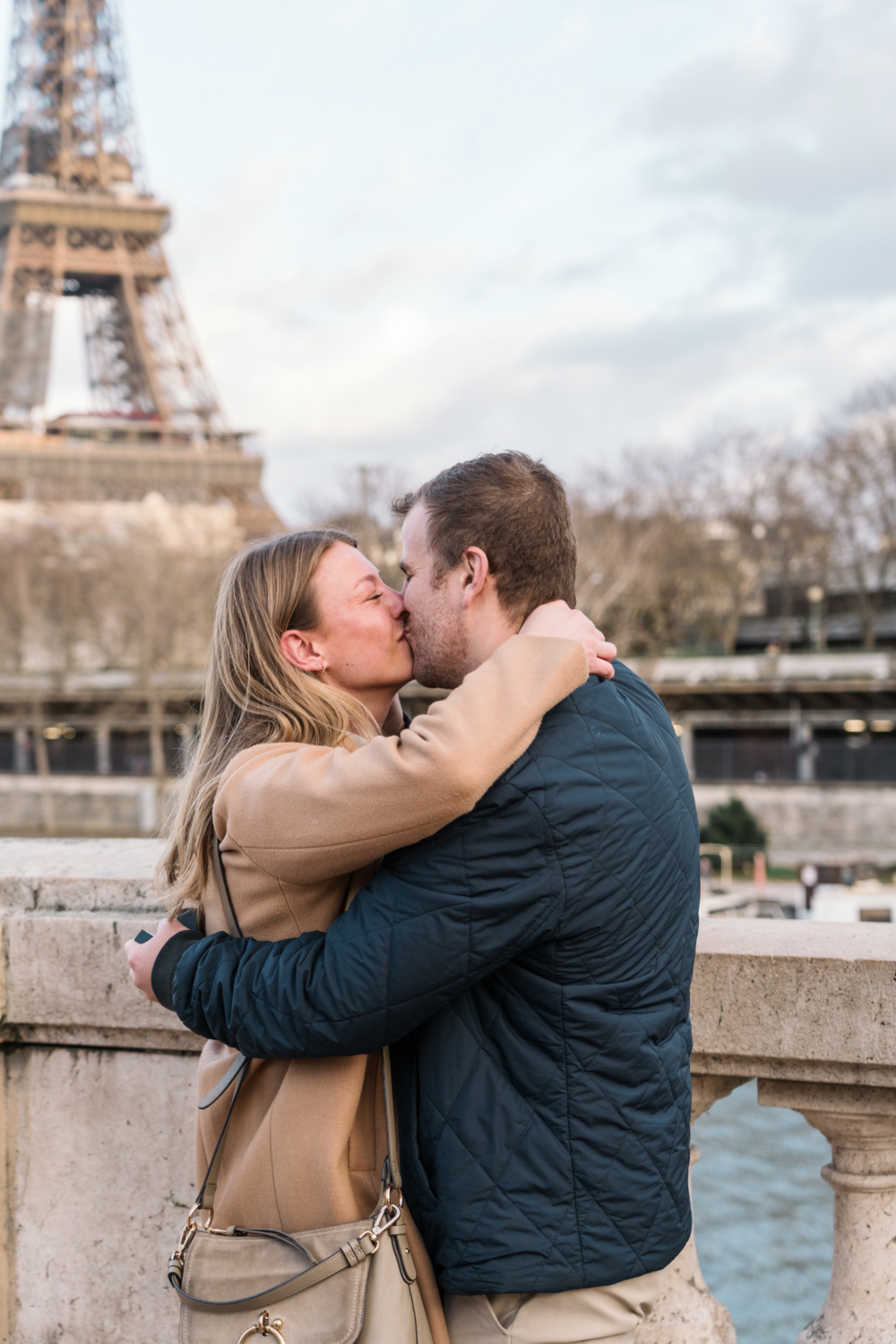 newly engaged couple kiss with view of eiffel tower after their surprise proposal