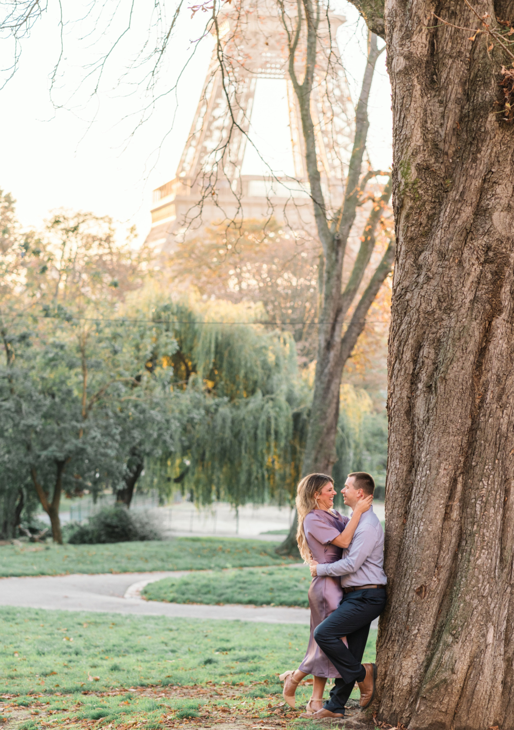 joyful couple pose in park in paris with view of eiffel tower