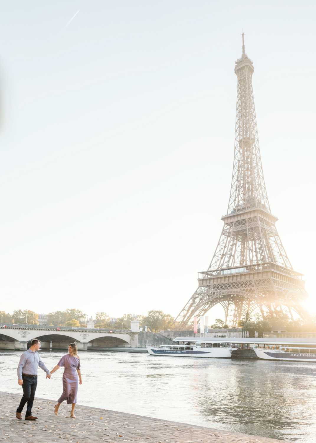 beautiful couple walk hand in hand as they walk along seine river in paris