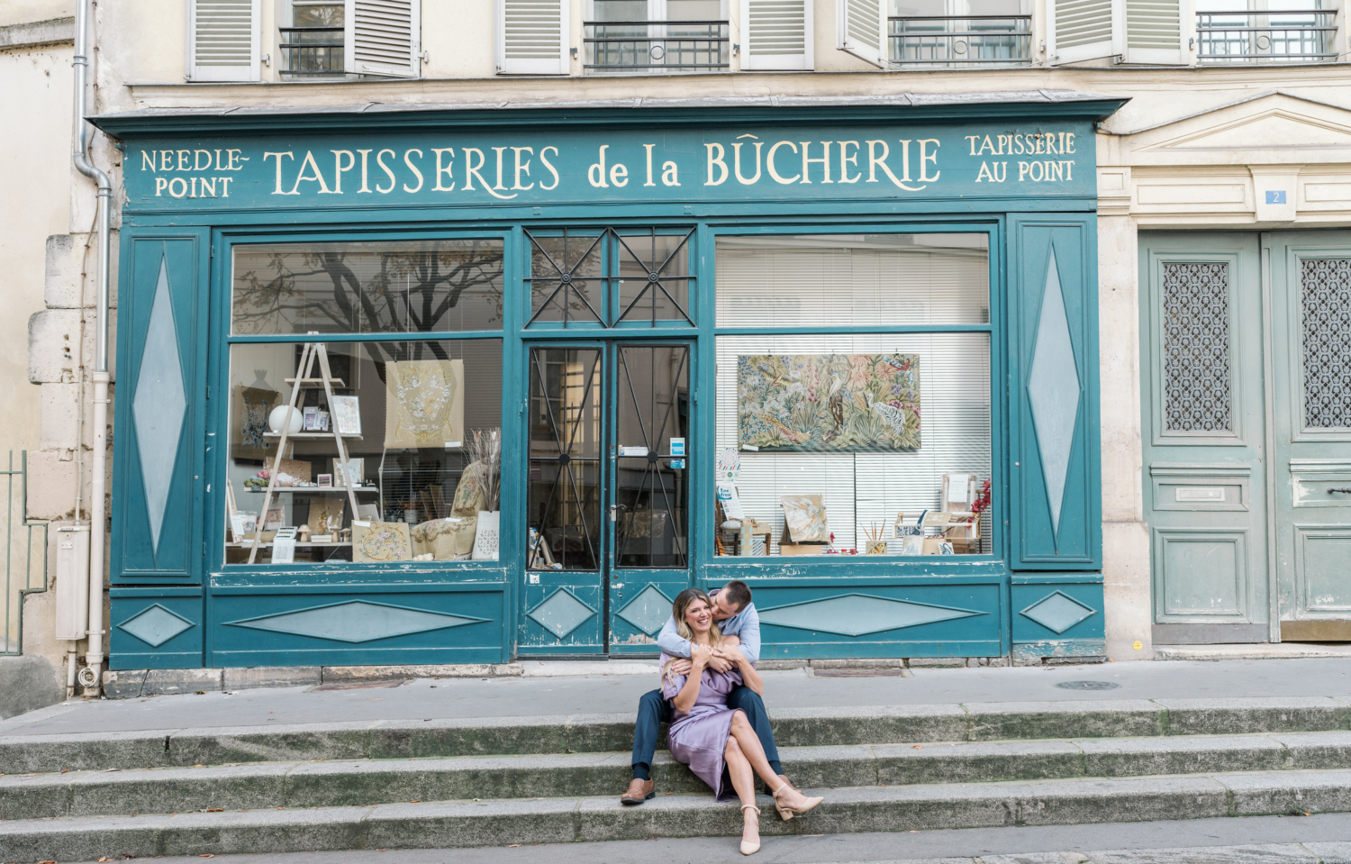 husband kisses wife on cheek in front of cute building in paris