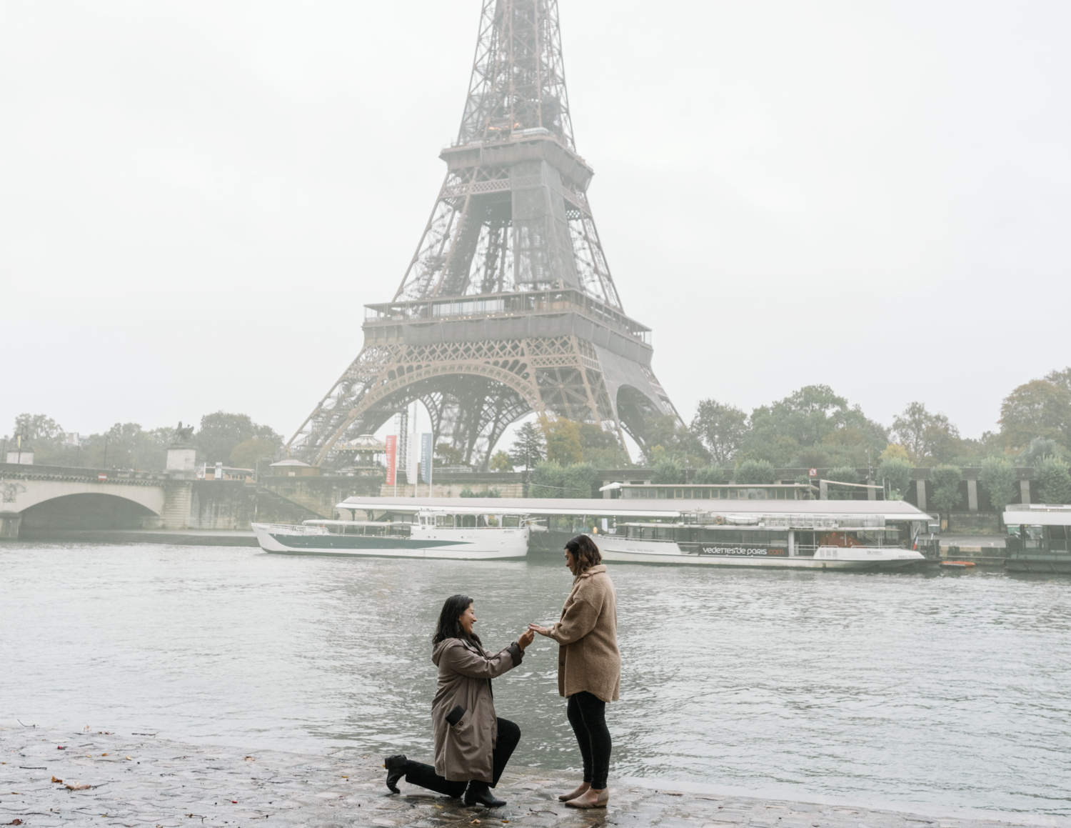 women on one knee presents diamond ring to another woman with view of the eiffel tower