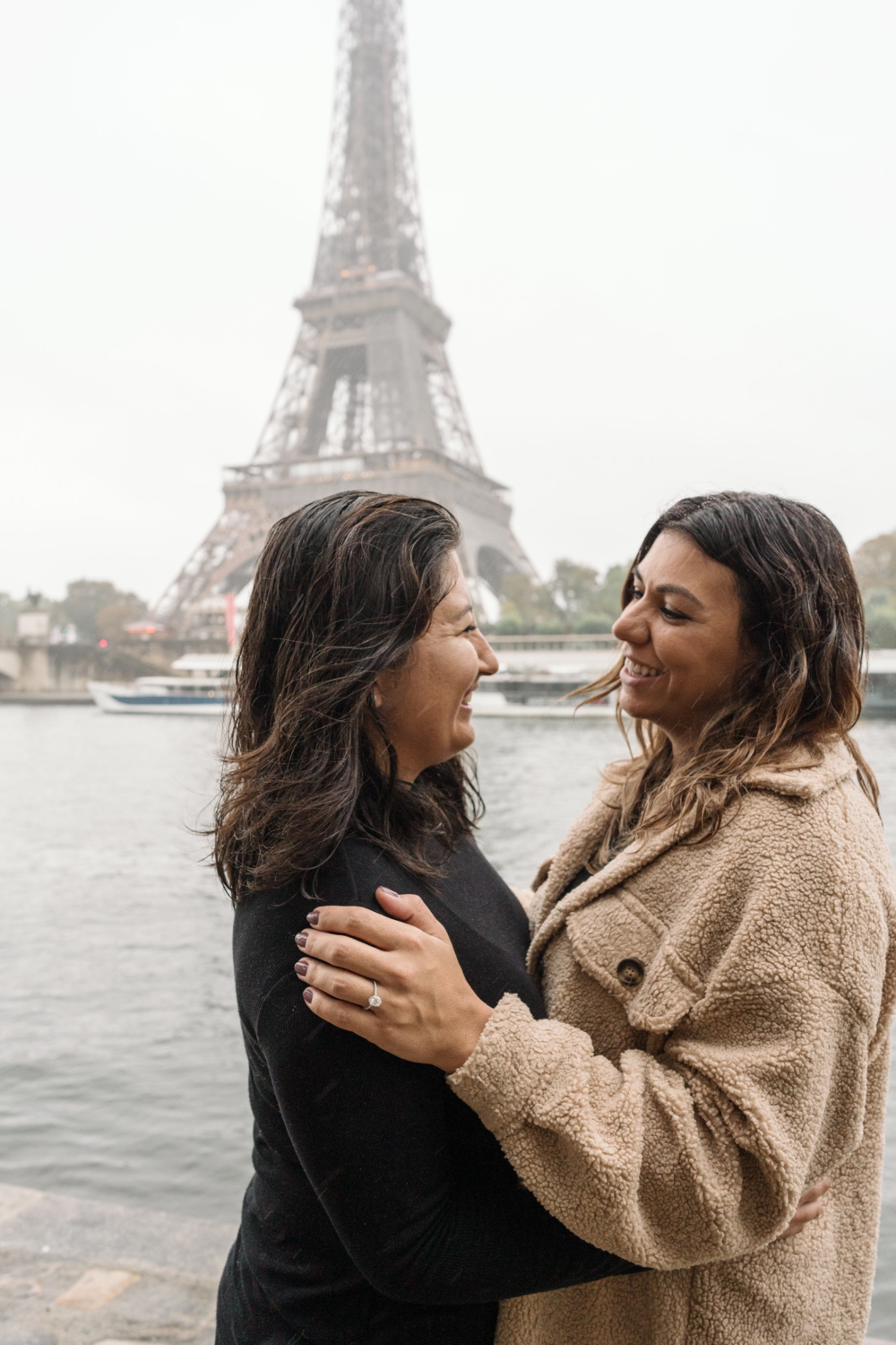 two women smile and laugh after their surprise proposal in paris wtih view of eiffel tower