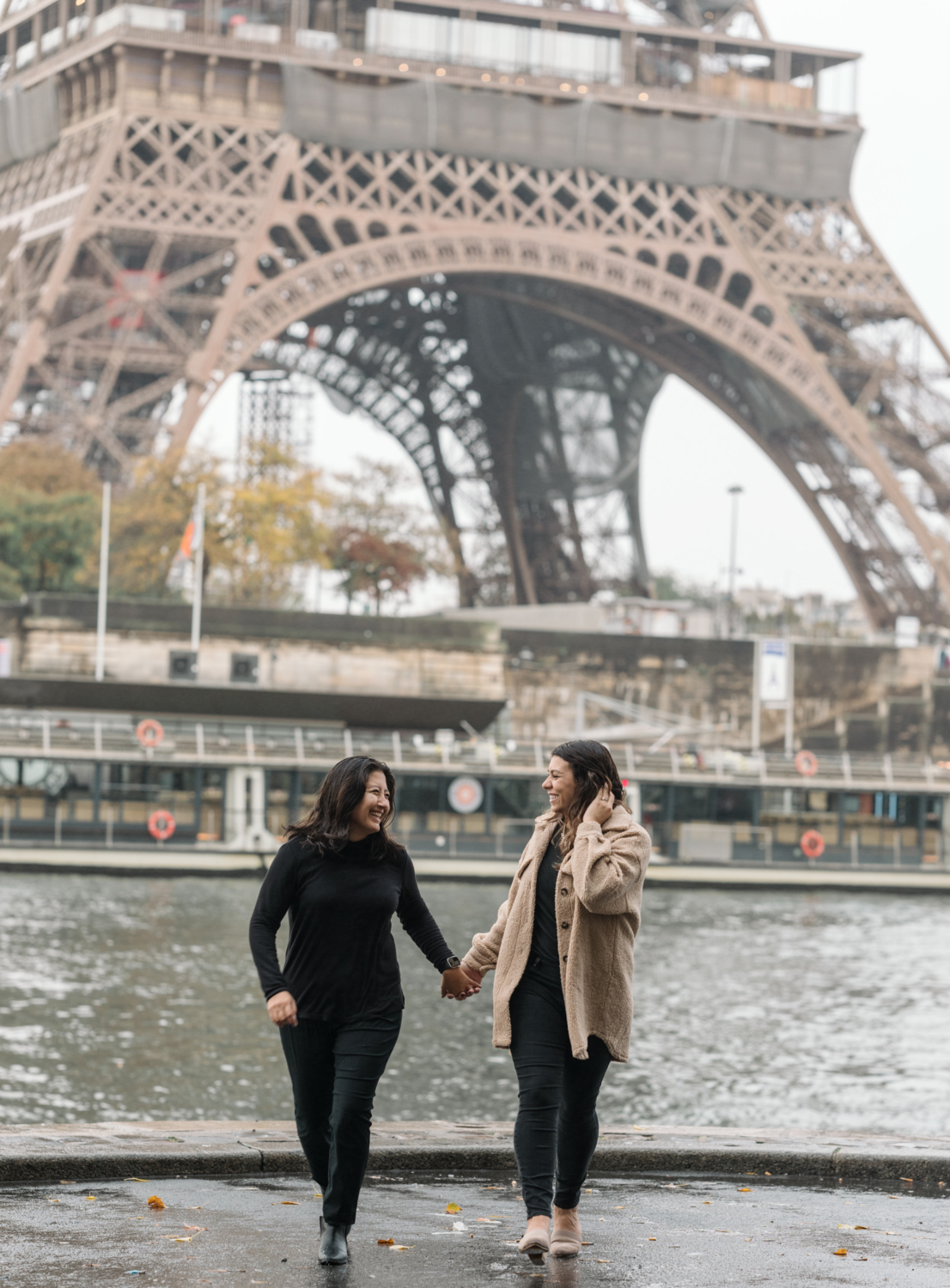 two women smile and laugh in paris with view of eiffel tower