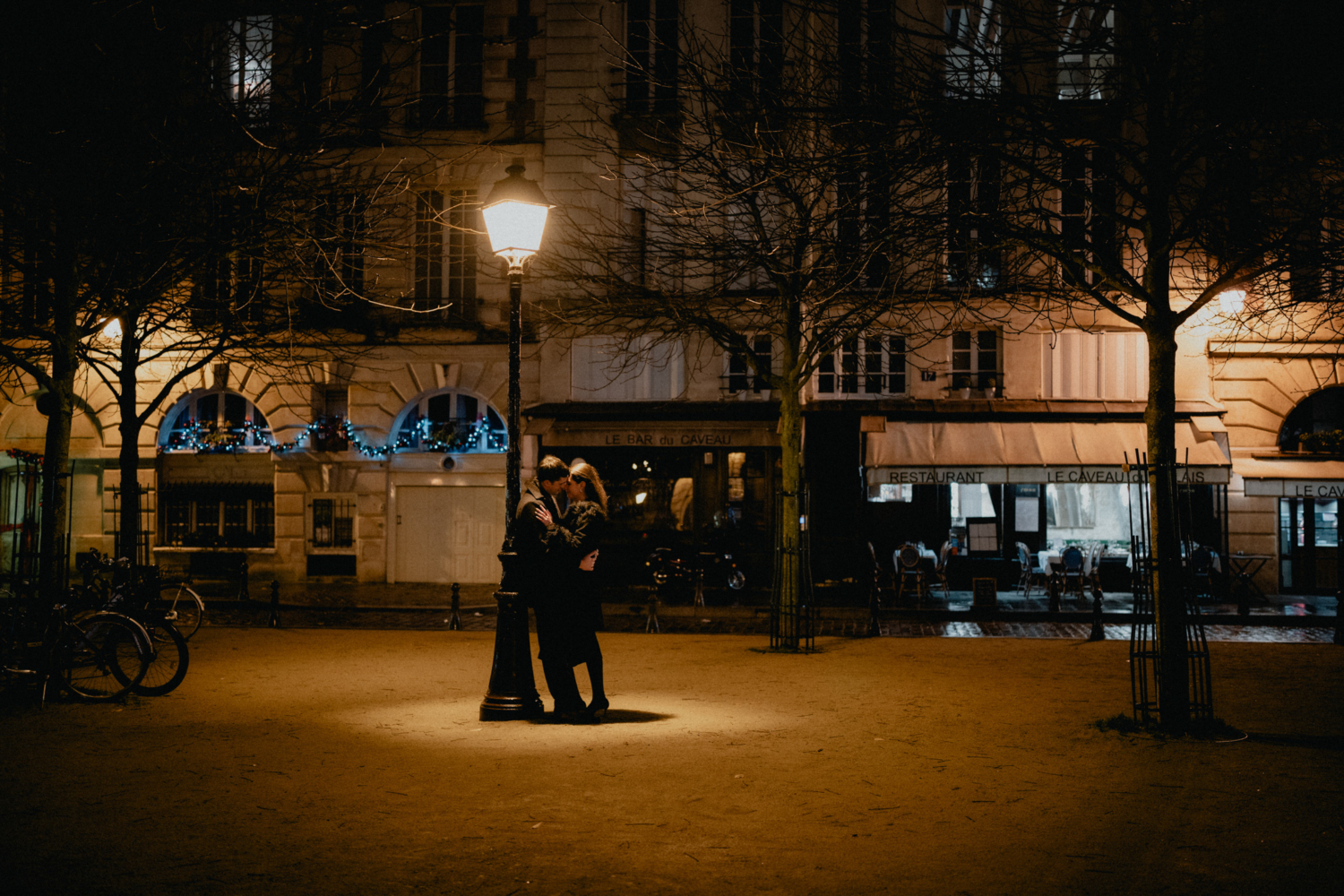 newly engaged couple embrace at place dauphine in paris at night time under a lamp