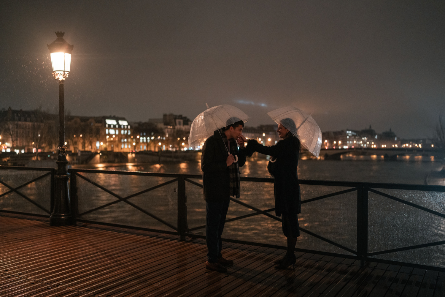 man kisses womans hand in the rain in paris at night