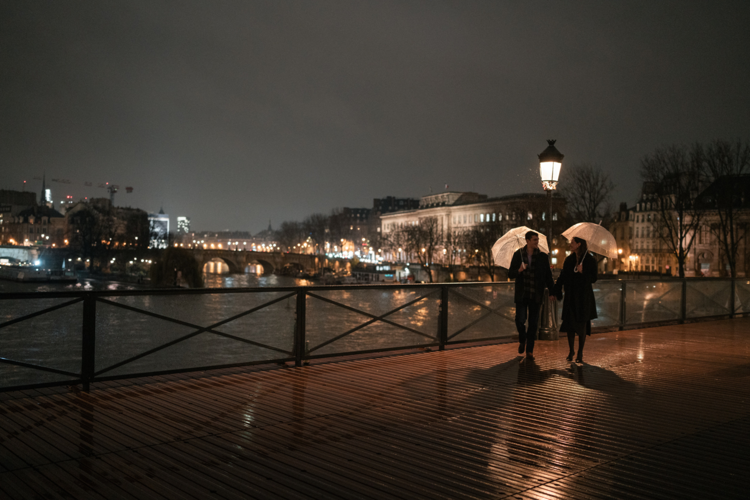 newly engaged couple walk hand in hand in the rain on pont des arts in paris