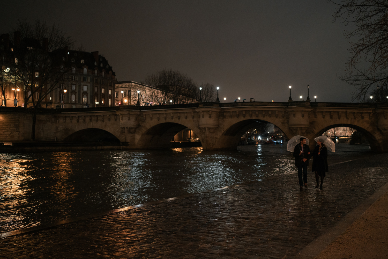 newly engaged couple walk along the banks of the seine river at night in paris