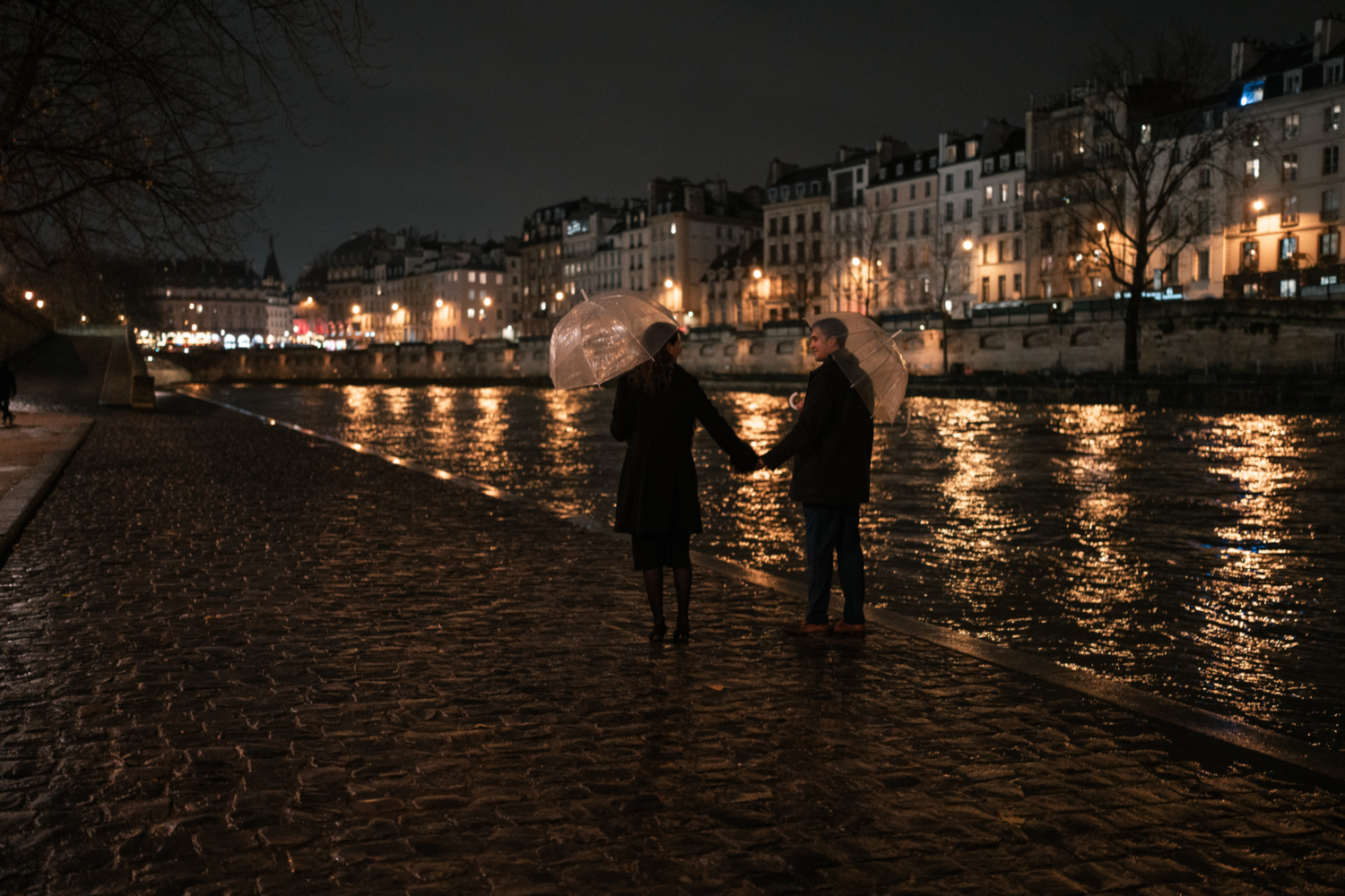 newly engaged couple walk along the seine river in the rain in paris