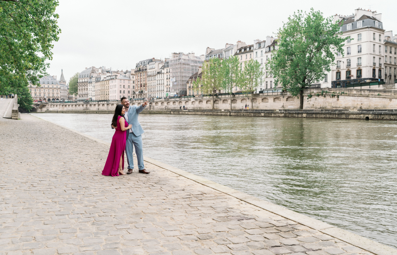 man points to something with woman as they walk along seine river in paris