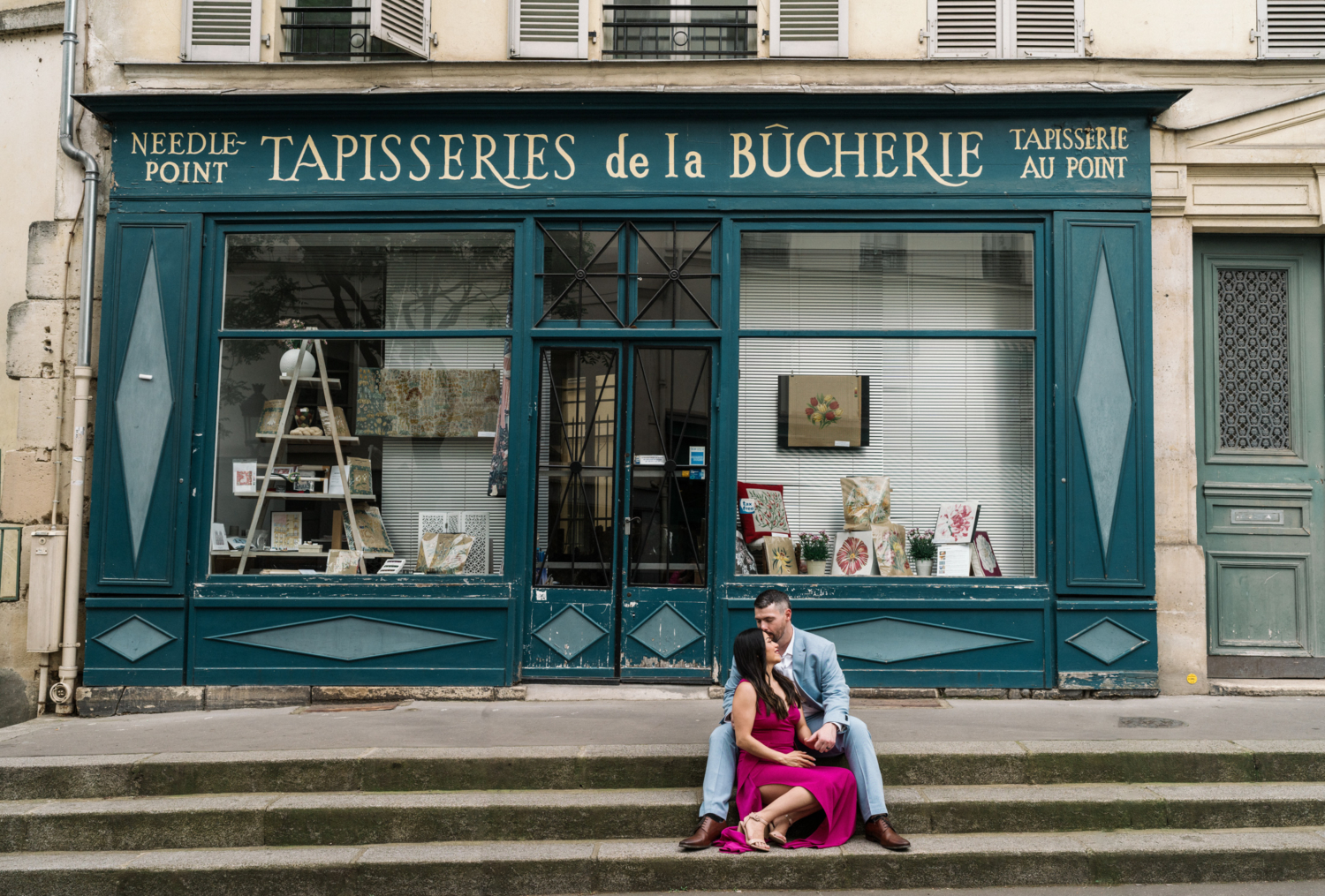 woman and man cuddle in front of needlepoint shop in paris