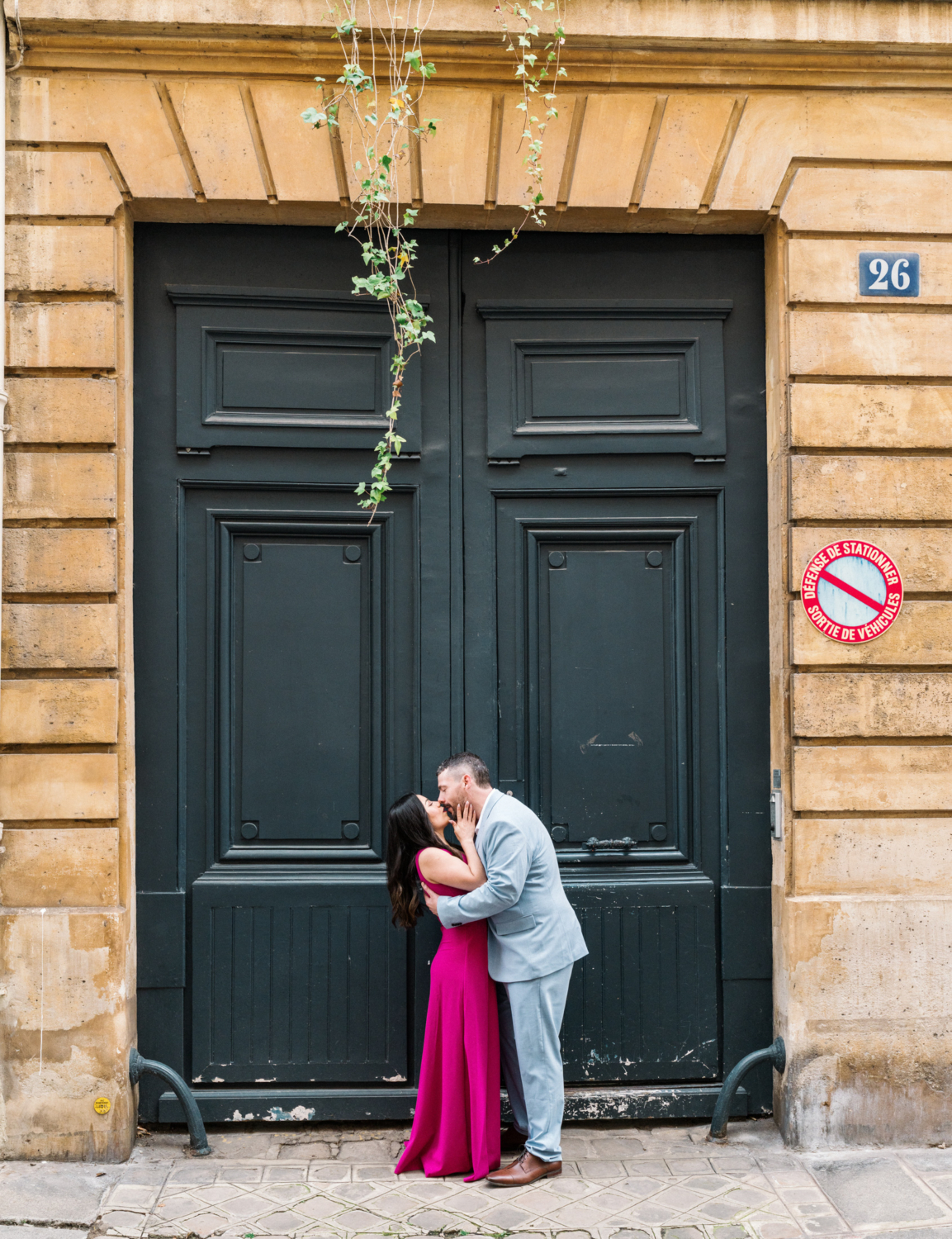 husband and wife kiss in front of large green door in paris france