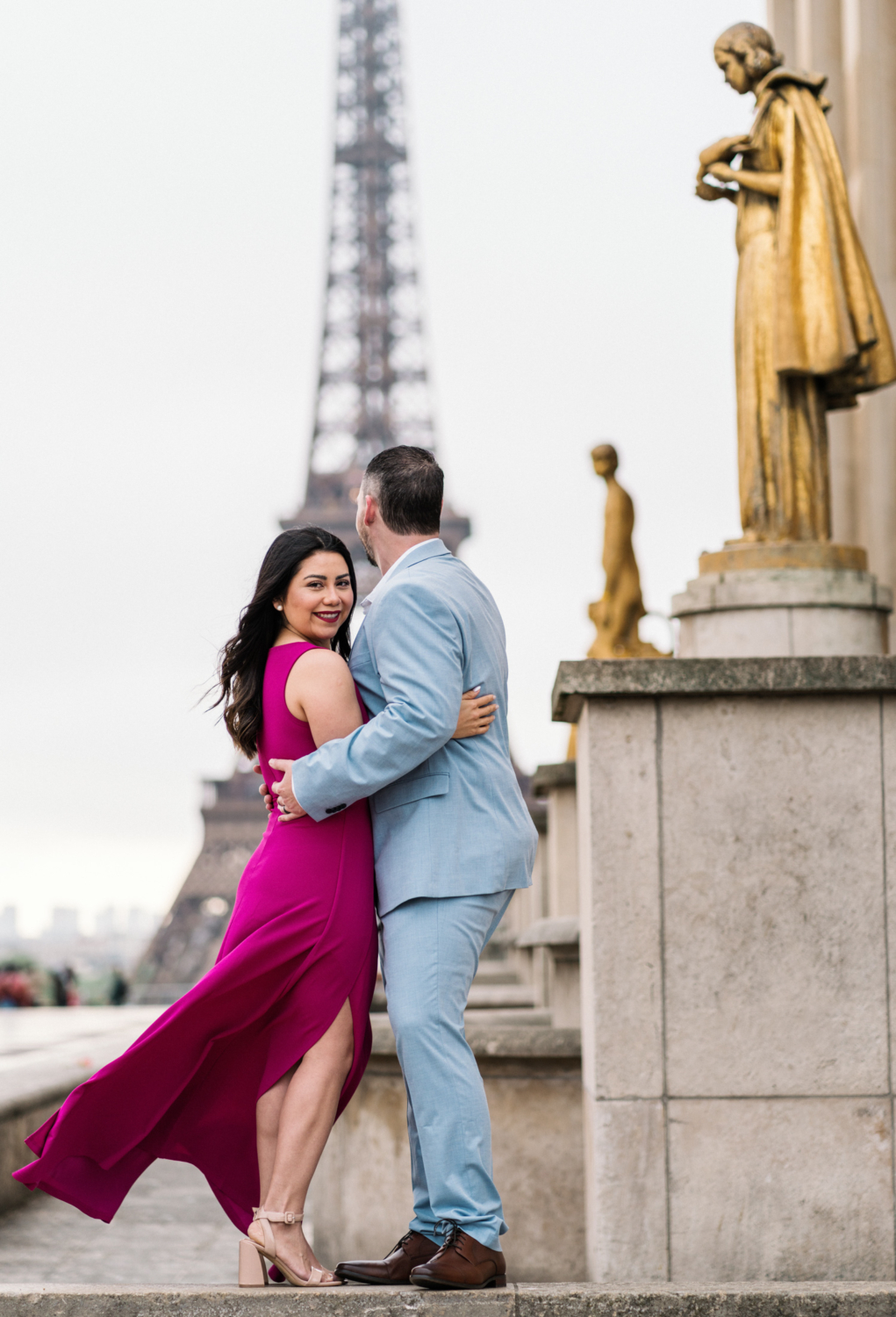 woman smiles as she holds on to her husband at eiffel tower paris