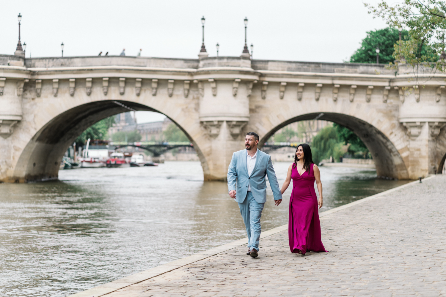 beautiful couple walk hand in hand next to pont neuf in paris