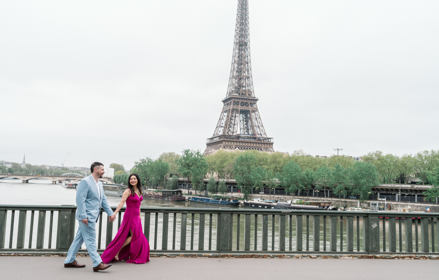 married couple walk along bridge in paris with view of eiffel tower