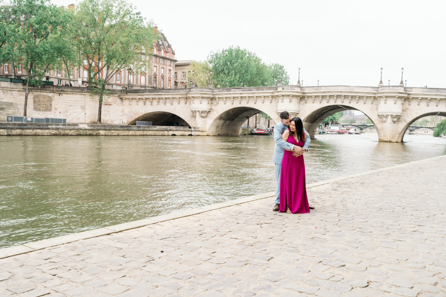 husband embraces wife with view of pont neuf in paris