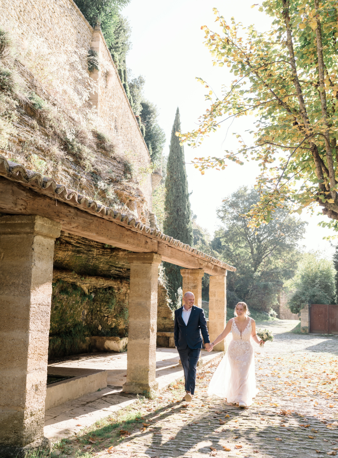 bride and groom walk next to old lavoir in gordes france provence