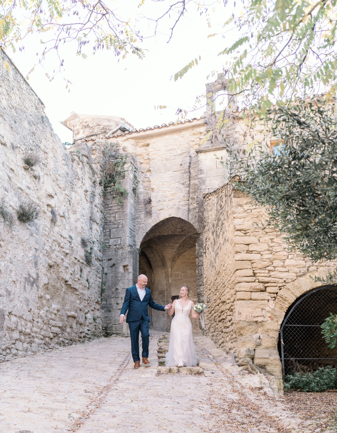 bride and groom walk through ancient gate in gordes france provence