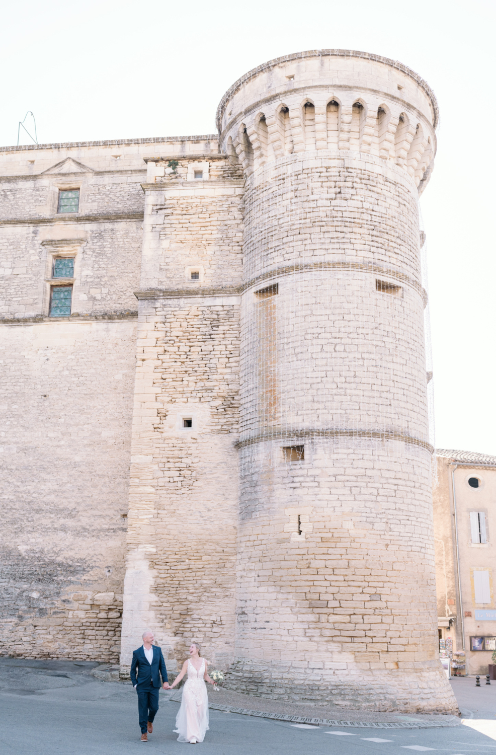 bride and groom laugh and walk next to castle on their wedding day in gordes france