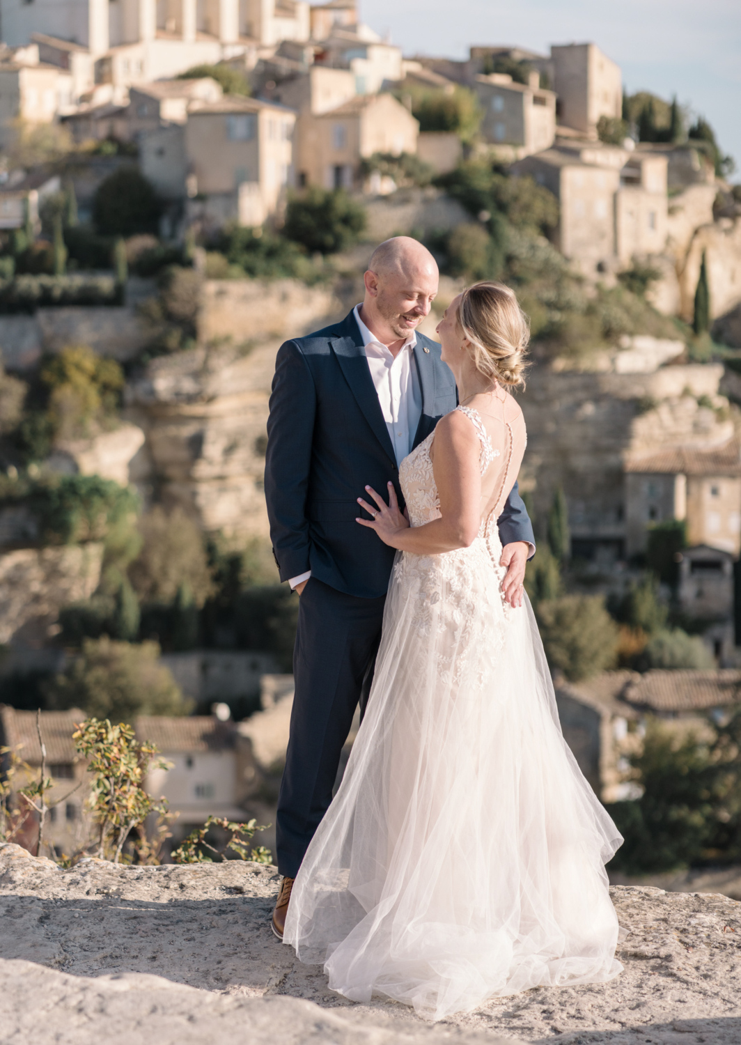 bride and groom smile at each other with gordes france in background