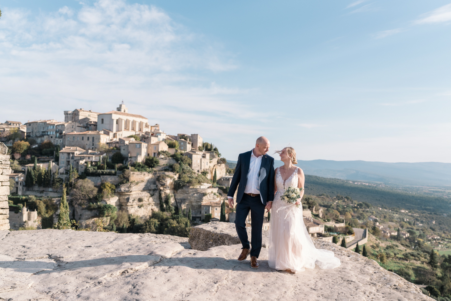 bride and groom walk in gordes france provence on a rock with view of village