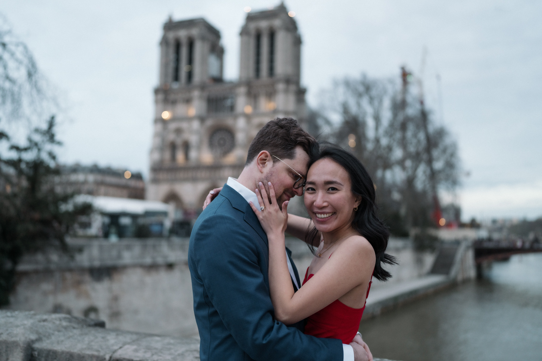 newly engaged couple embrace with view of notre dame cathedral in paris