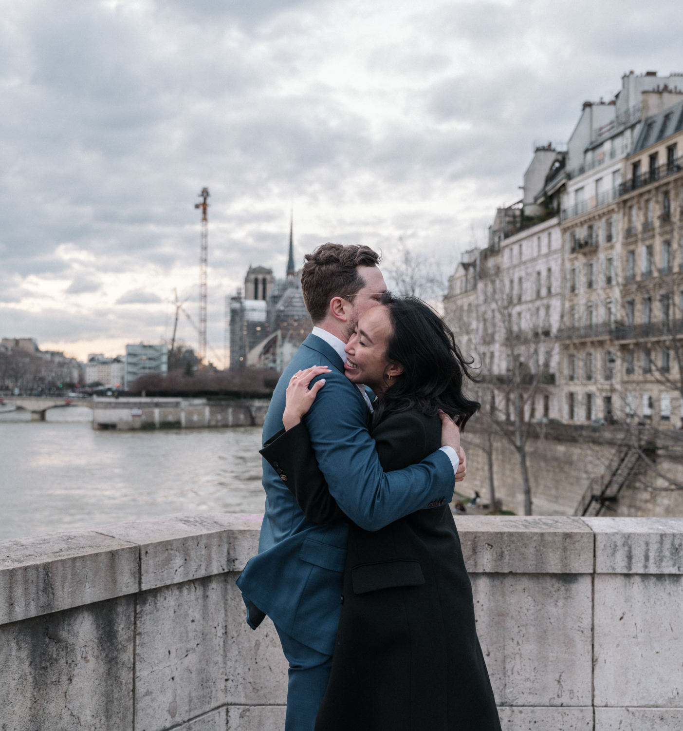 woman embraces man after surprise proposal in paris with view of notre dame