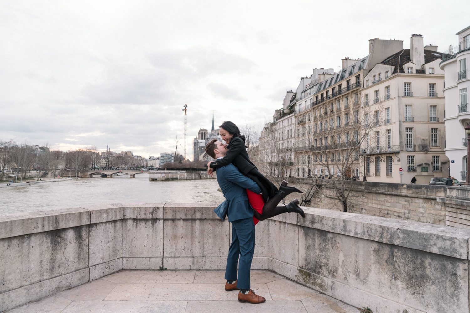 man lifts woman after engagement in paris with view of notre dame