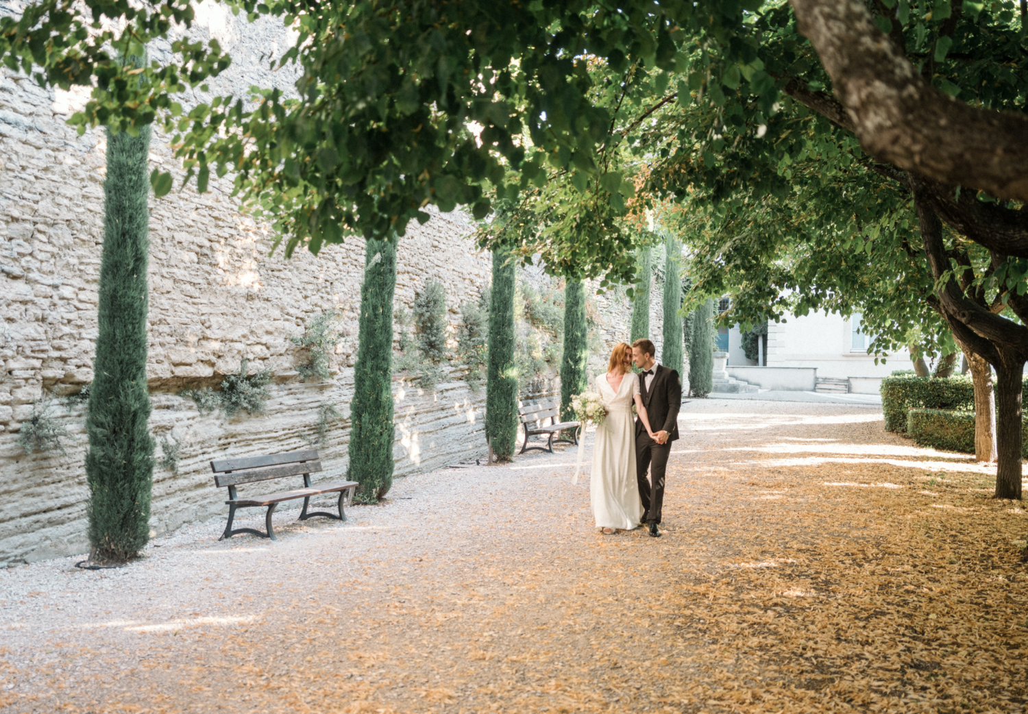 bride and groom walk through a garden with green trees in gordes france