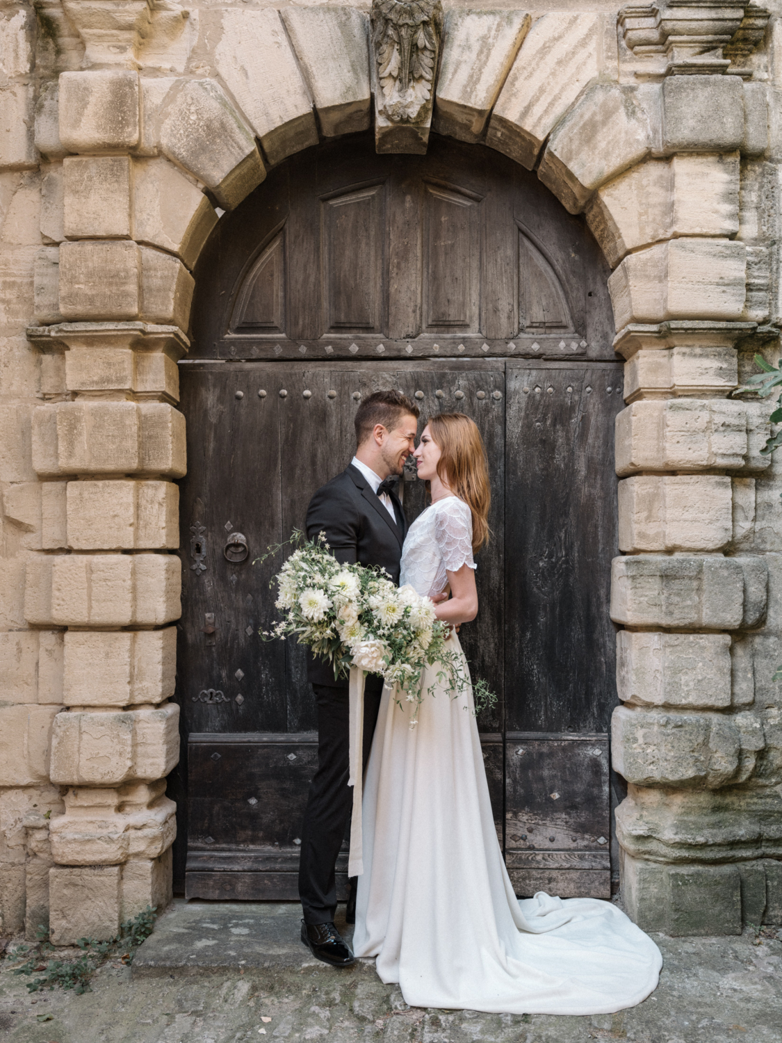 bride and groom stand in front of brown door in gordes france during their La Bastide de Gordes wedding