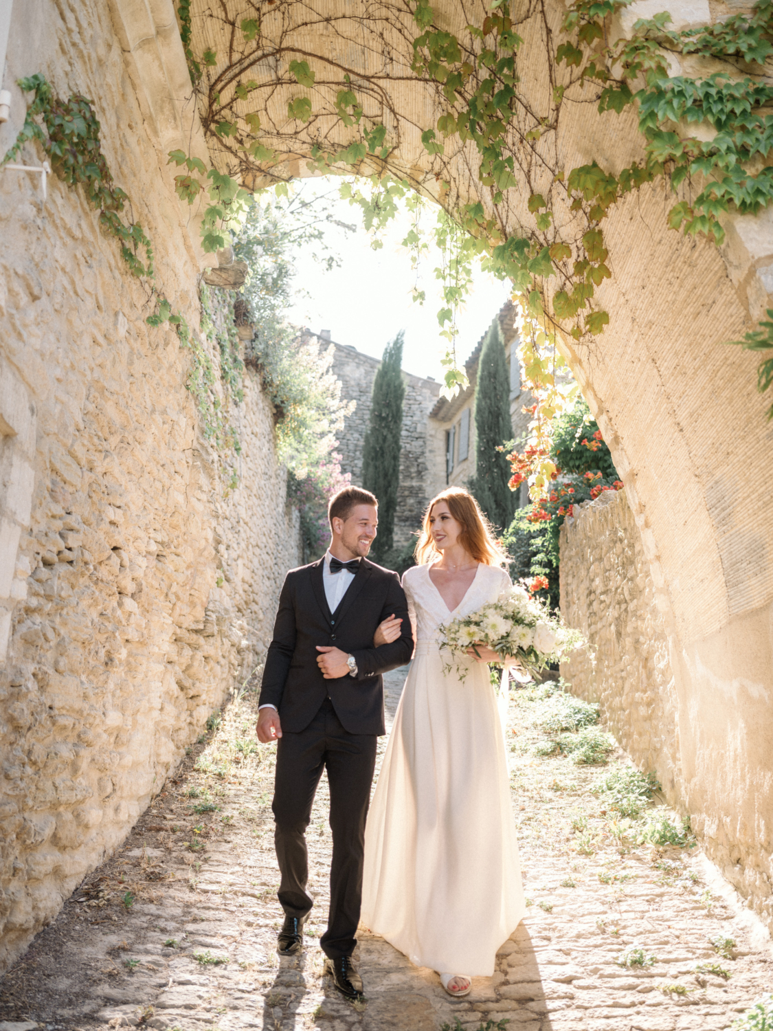 bride and groom walk arm in arm down cobblestone path in gordes france during their La Bastide de Gordes wedding