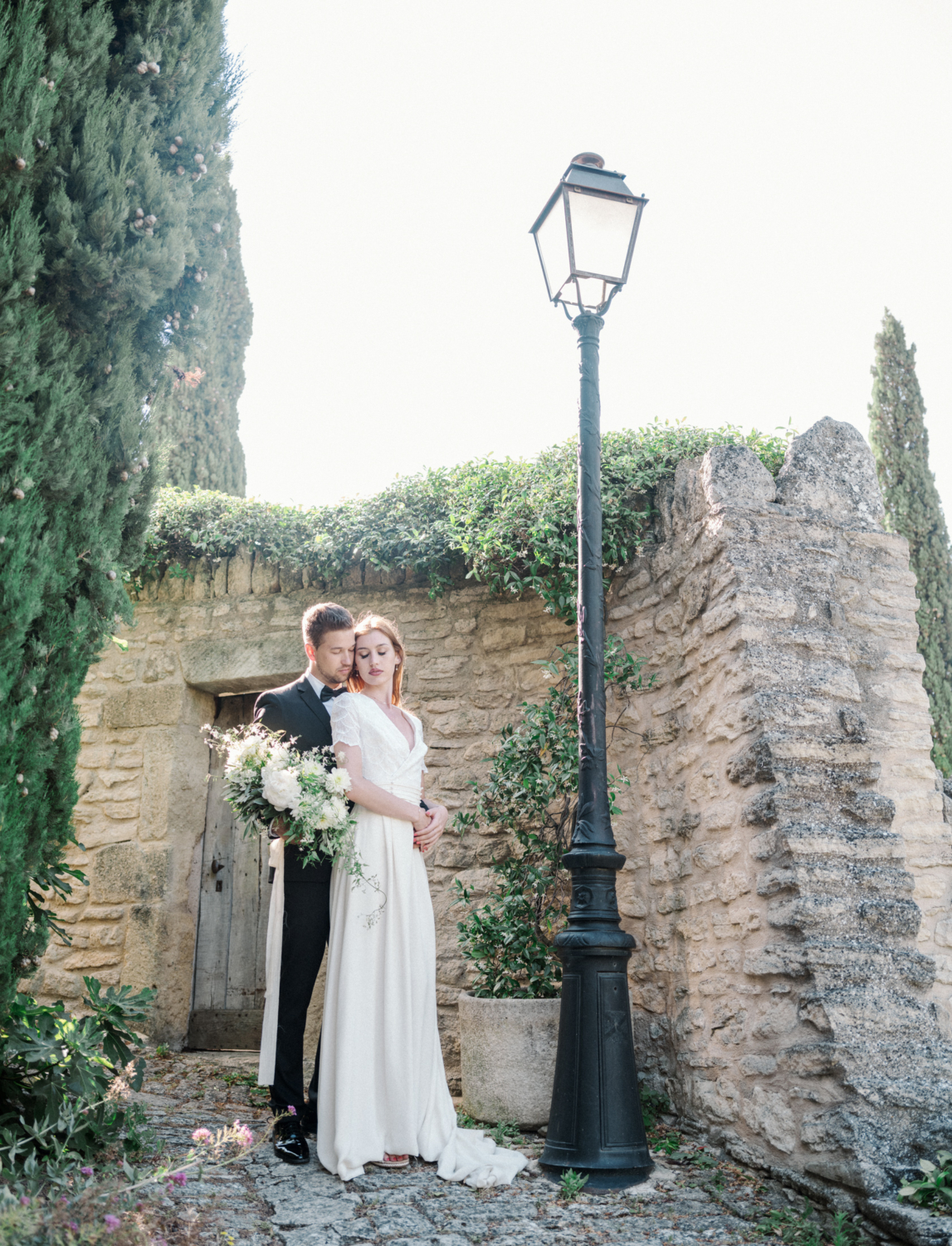 bride and groom embrace elegantly in front of lamp post in gordes france