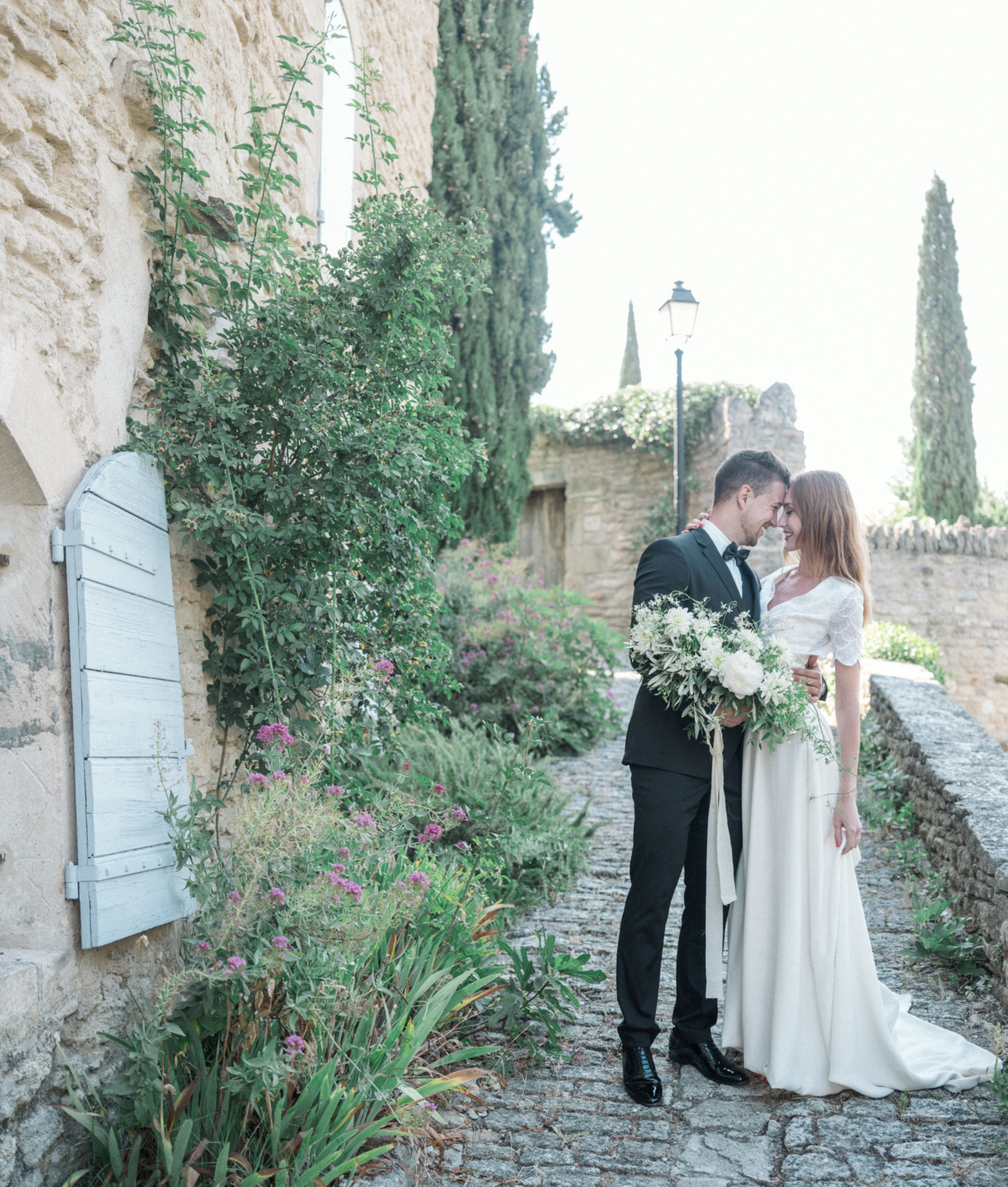 bride and groom smile at each other as they pose on a cobblestone path in gordes france