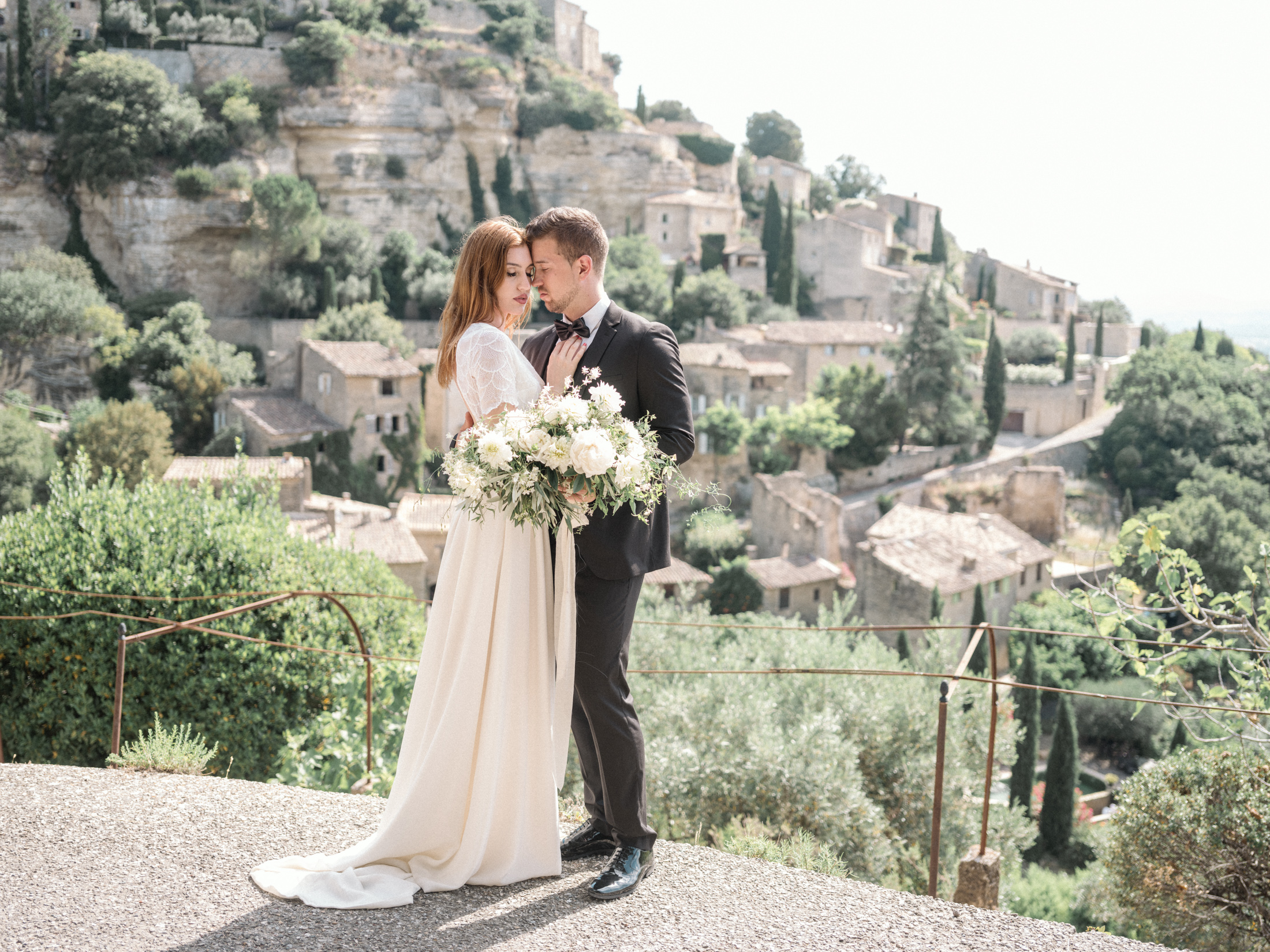 bride and groom embrace with magnificent view of gordes village in background