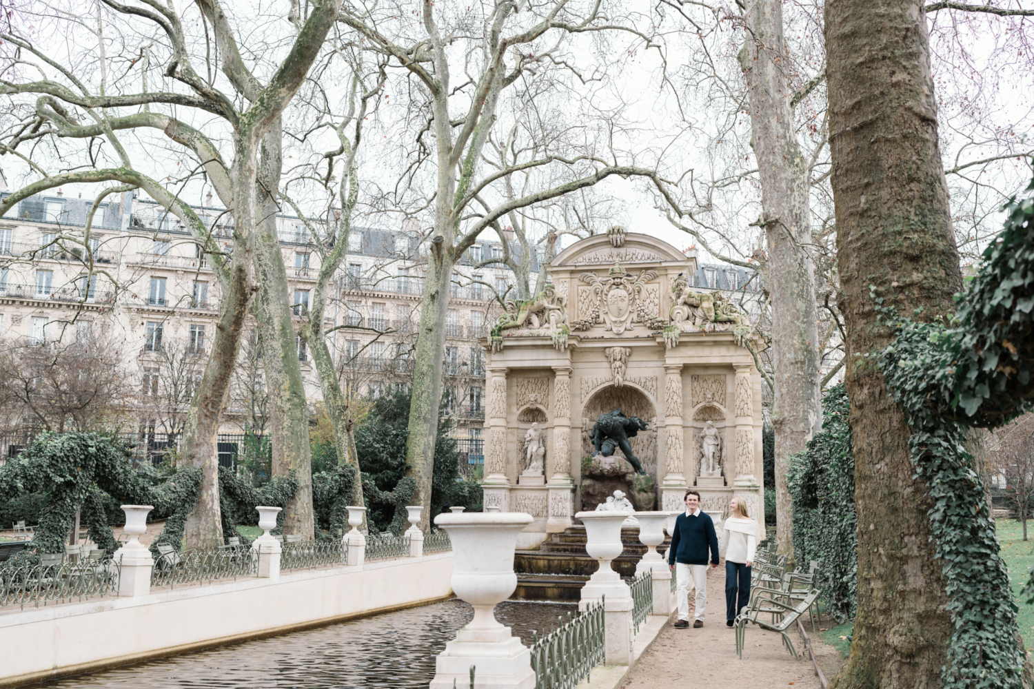 newly engaged couple walk through luxembourg gardens in front of medicis fountain in paris