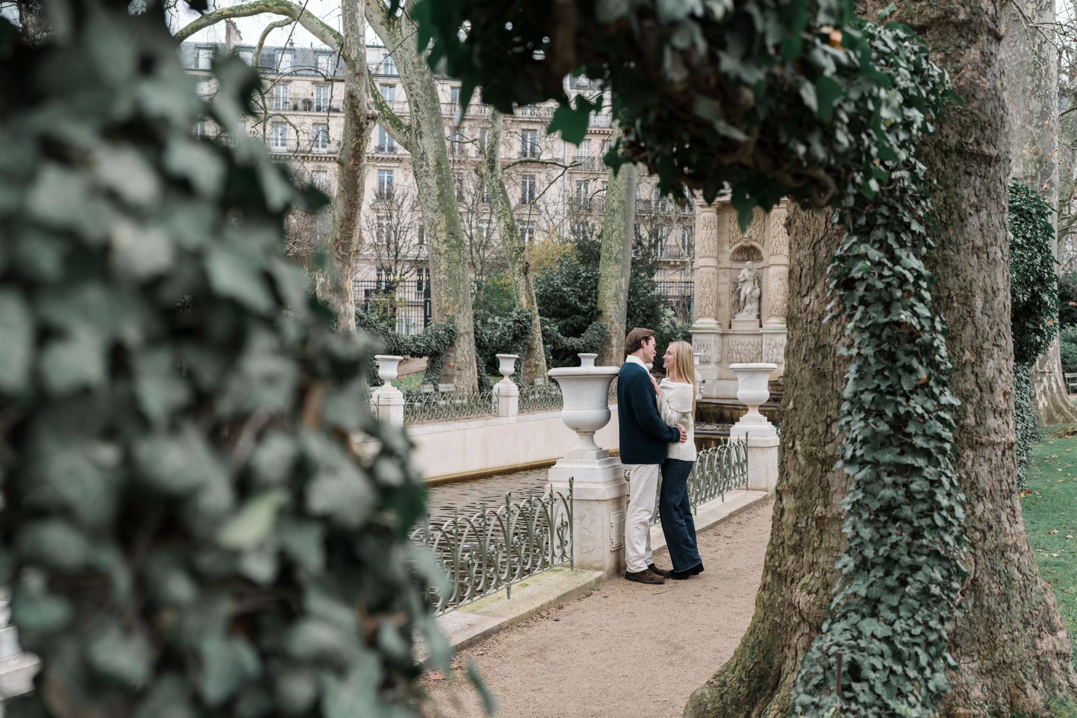 newly engaged couple embrace in luxembourg gardens in paris with view of ivy