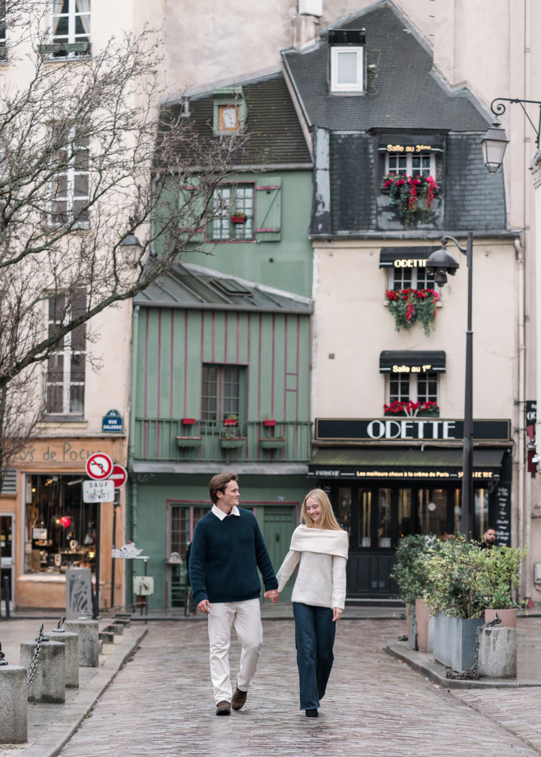 newly engaged couple walk through charming parisian neighborhood with odette restaurant in background