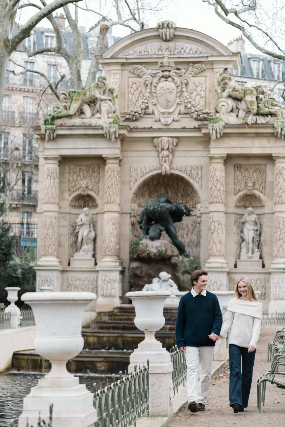 newly engaged couple walk hand in hand at medicis fountain in paris