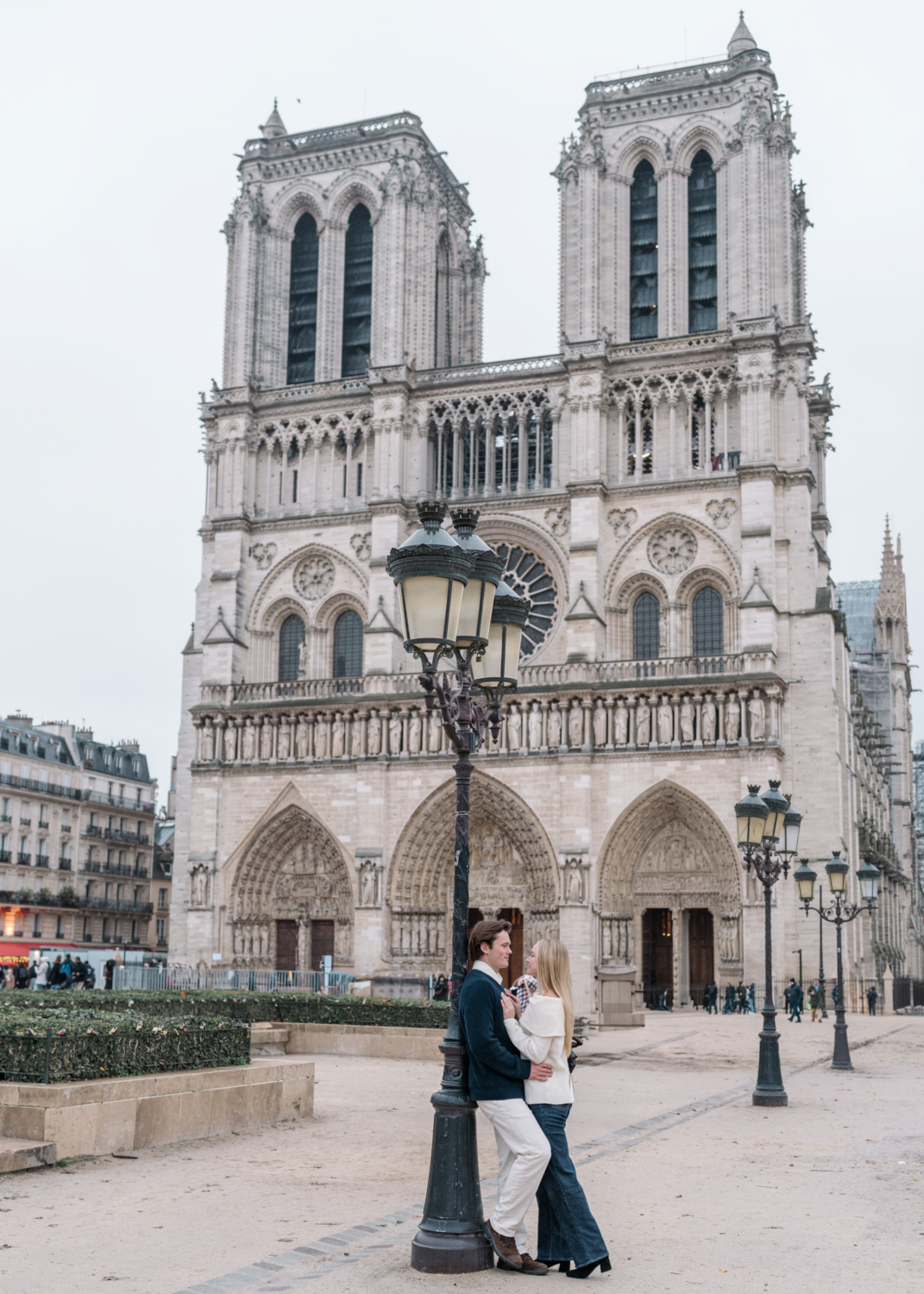 newly engaged couple embrace in front of notre dame cathedral in paris