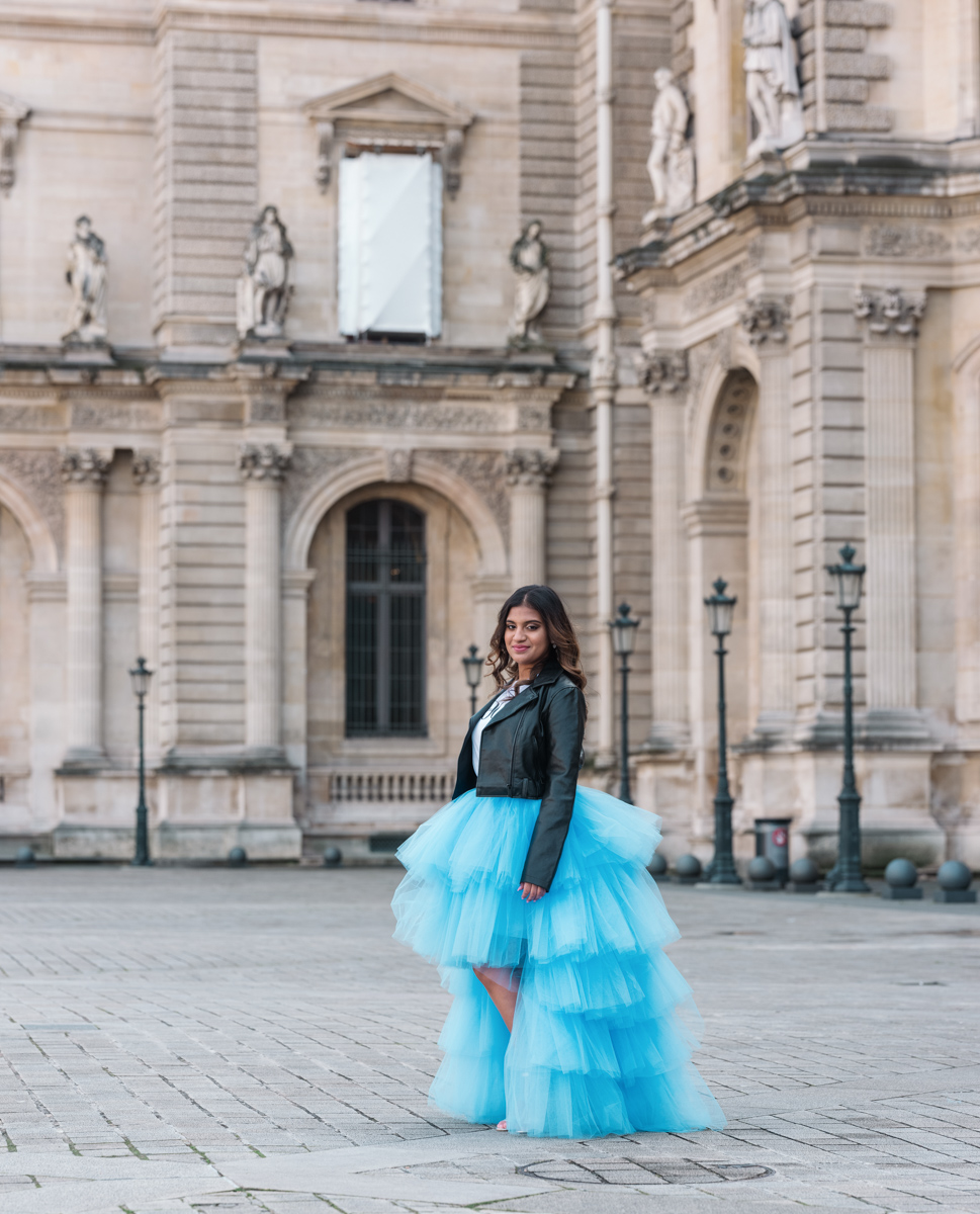 young woman in a blue dress poses at the louvre in paris