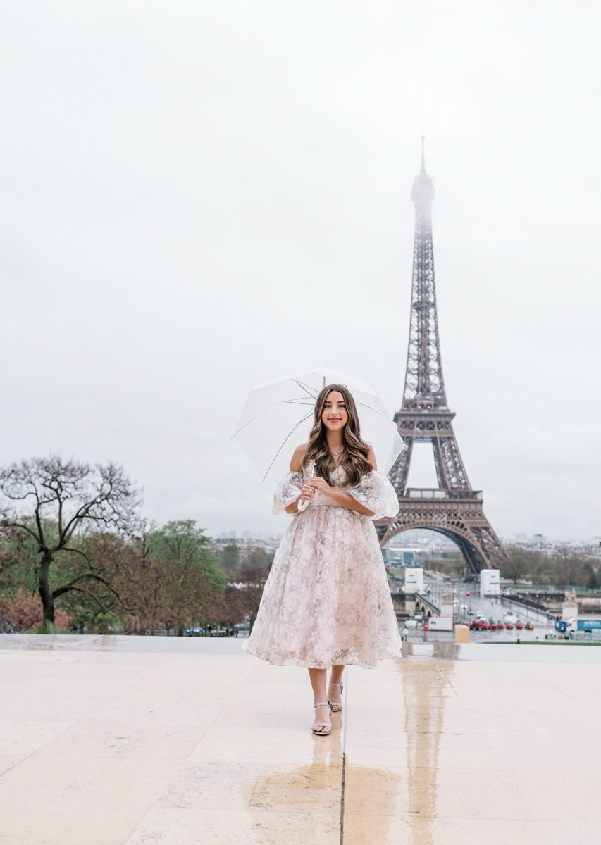 young woman walks with umbrella in front of eiffel tower