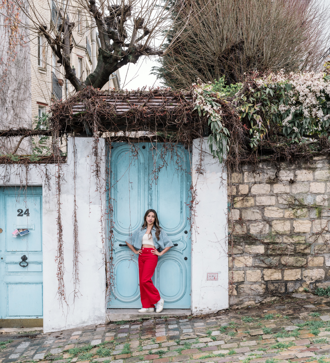 young woman in red pants poses in front of blue door in paris