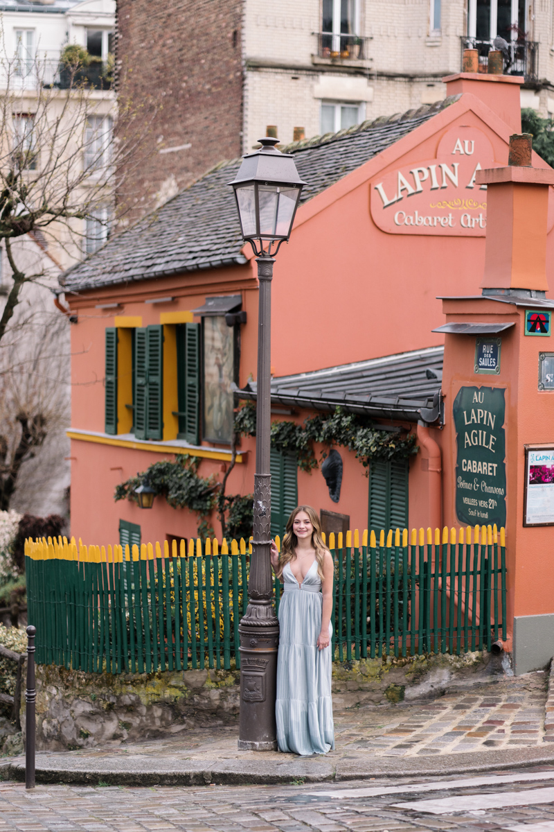 young woman poses in front of orange house in montmartre paris