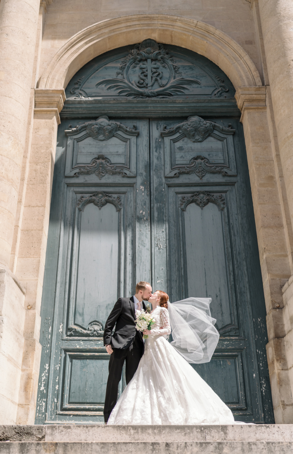 bride and groom kiss on the steps of saint roch church in paris