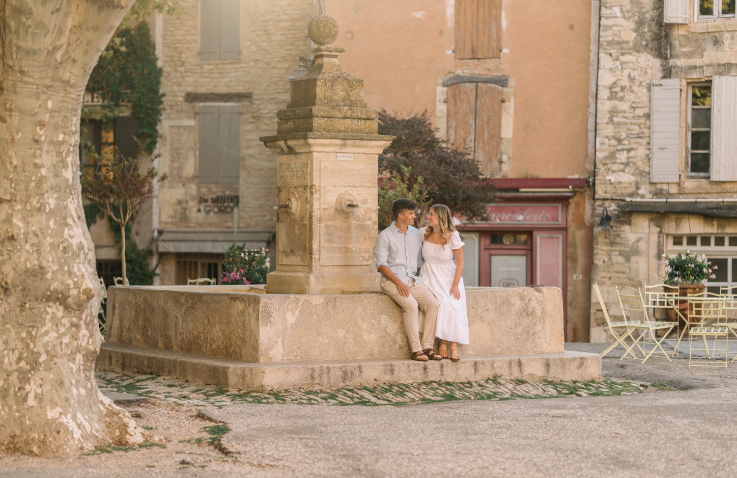 engaged couple sit next to fountain in gordes, provence france