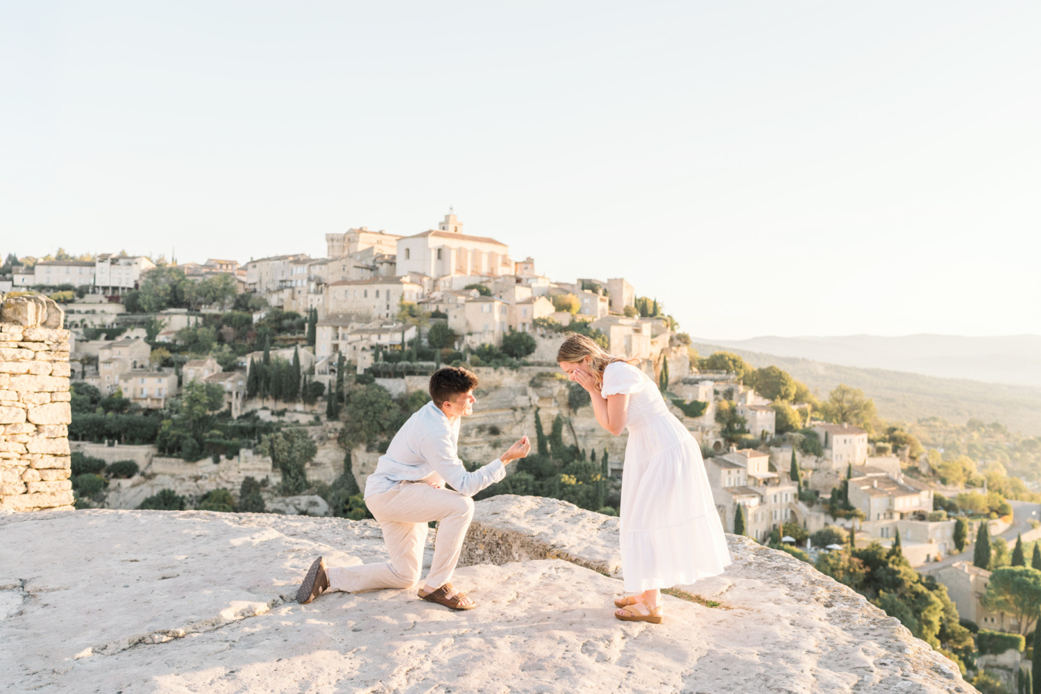 woman holds her cheeks as her boyfriend proposes to her in gordes provence france