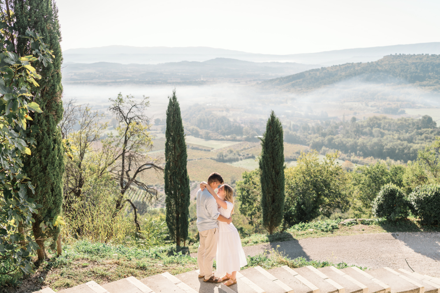 engaged couple embrace in front of cypress trees in gordes, provence, france