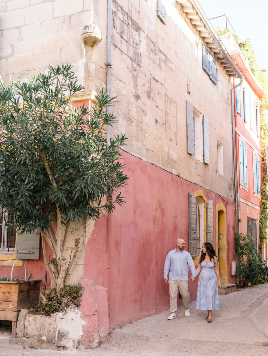 cute couple walk hand in hand in front of pink building in arles france